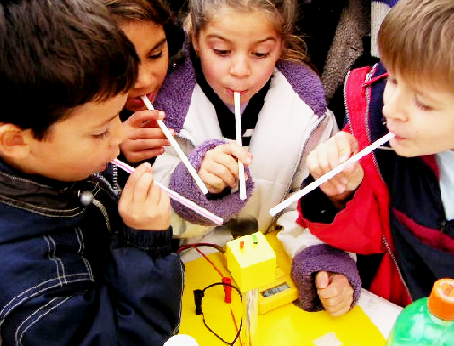 Pictogramme pour Groupe d'enfants entourant une expérience numérique et 
                souflant sur un capteur avec des pailles